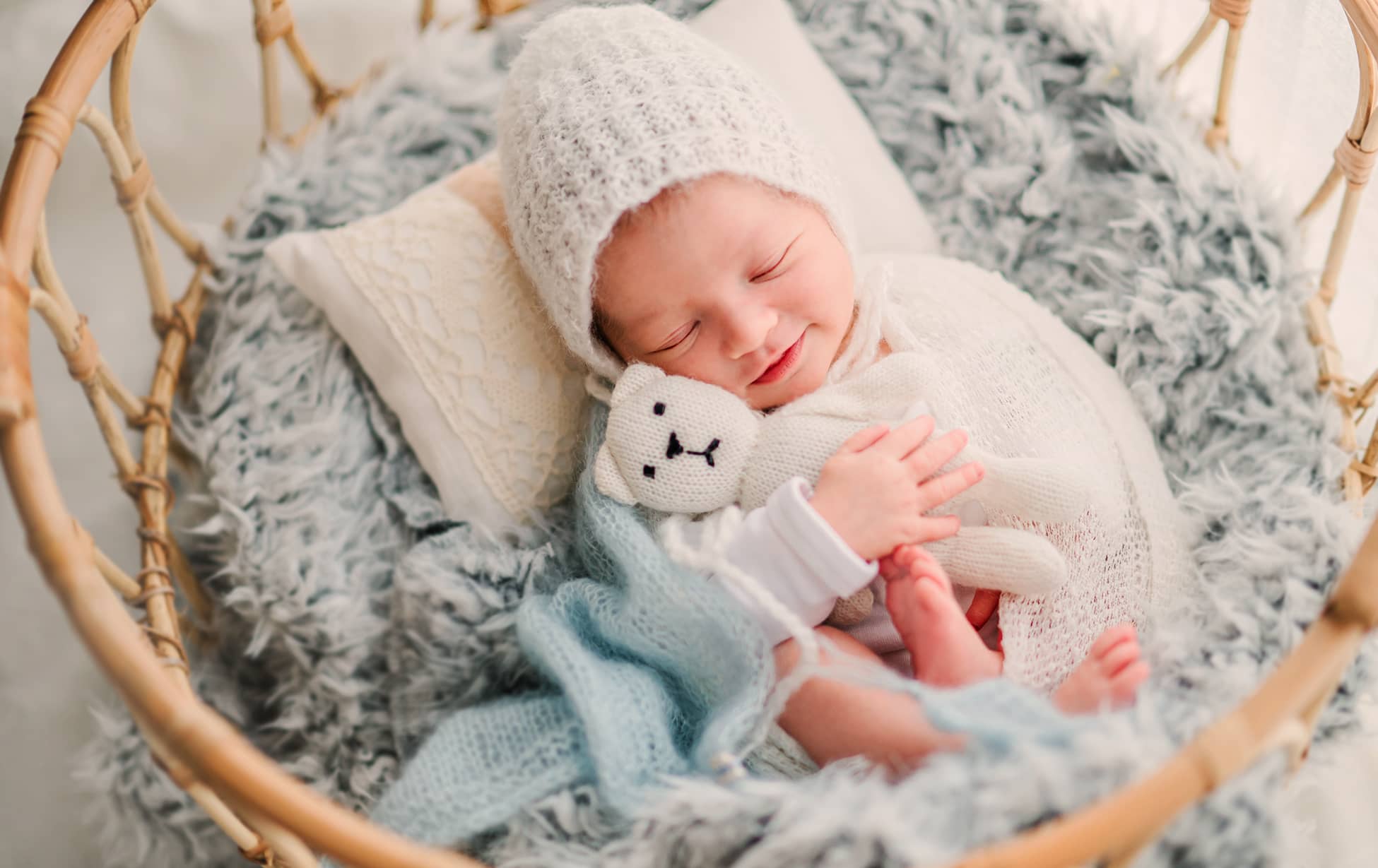 Sleeping baby with a knitted hat and soft toy in a cushioned basket