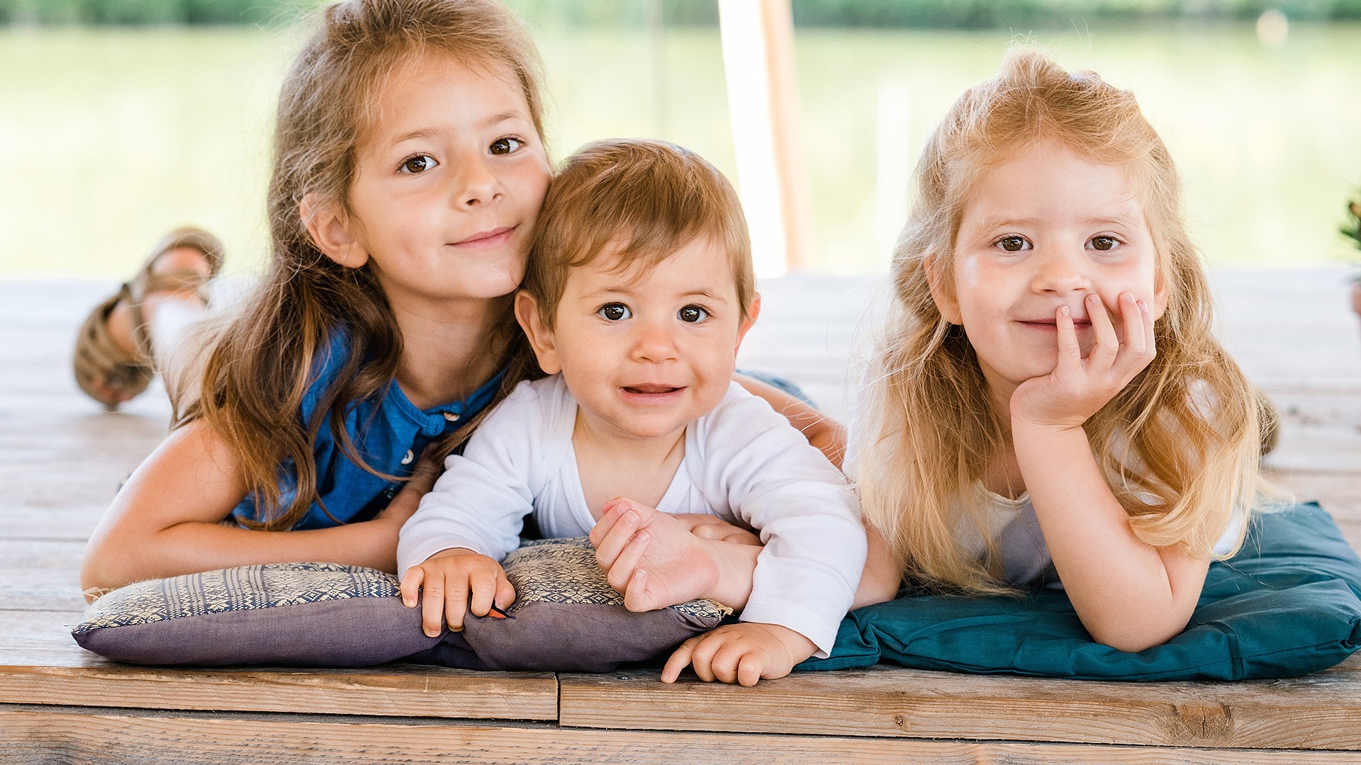 Three children lying side by side on a wooden table and looking at the camera