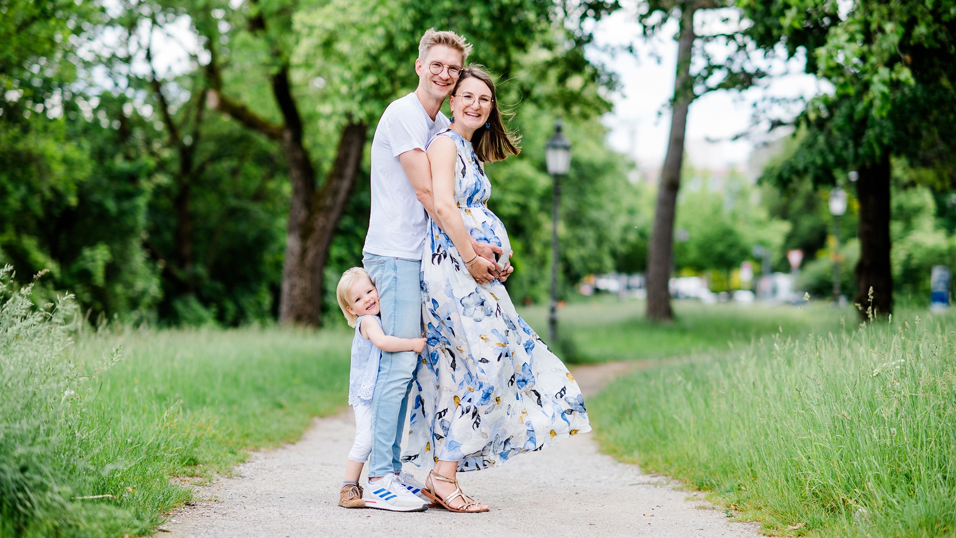 Family with a young child on a park path, with the mother wearing a floral dress