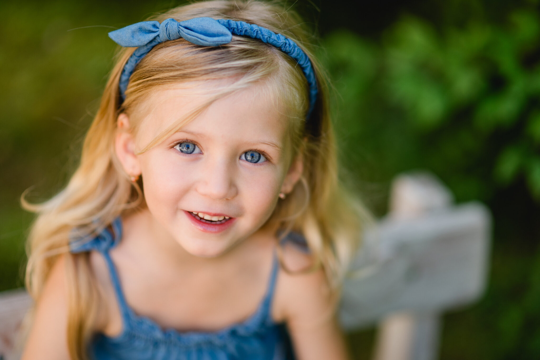 Child with a blue hair bow sitting in a garden and looking at the camera