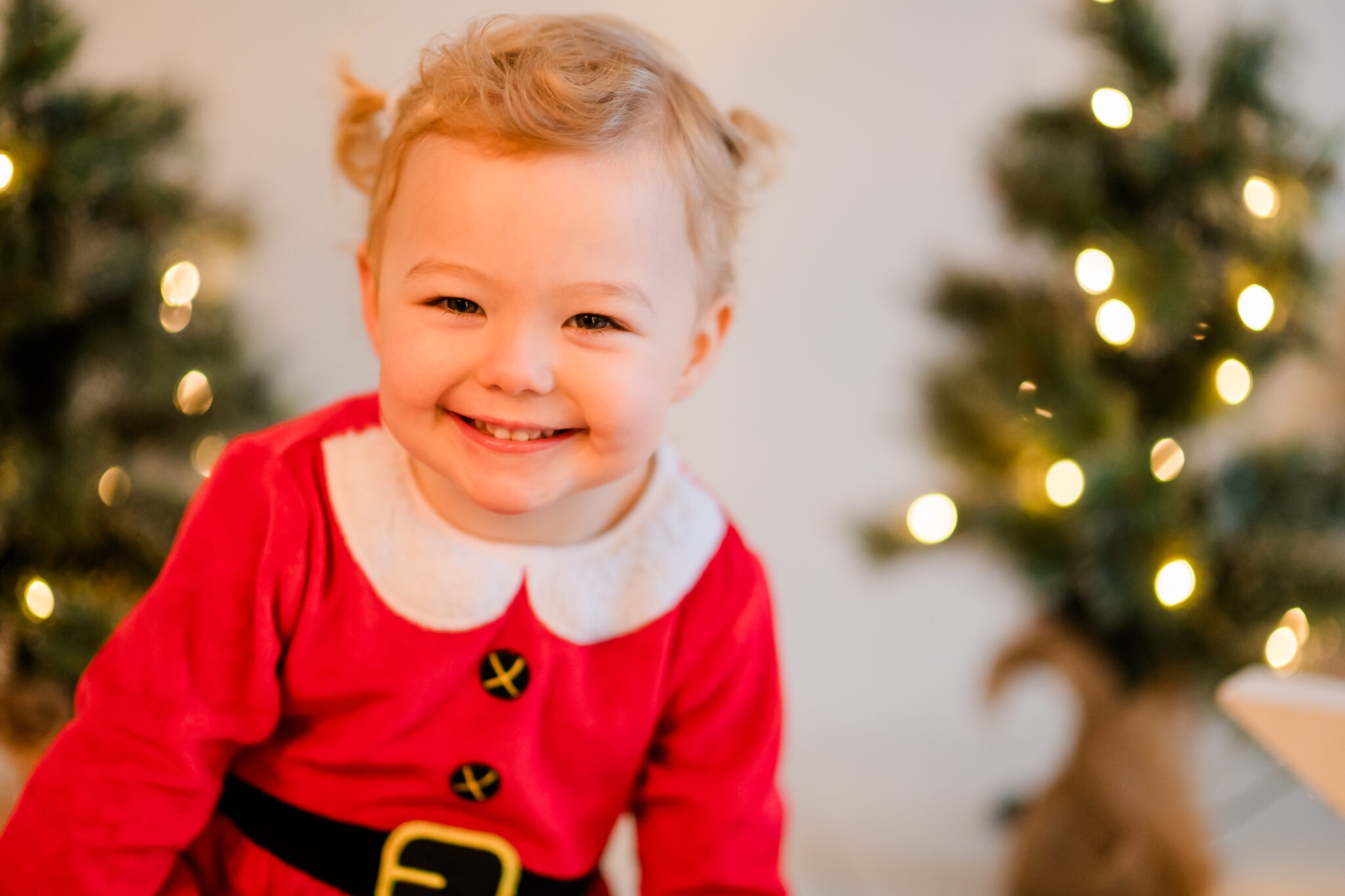 Smiling toddler in a red Christmas outfit in front of a tree with lights