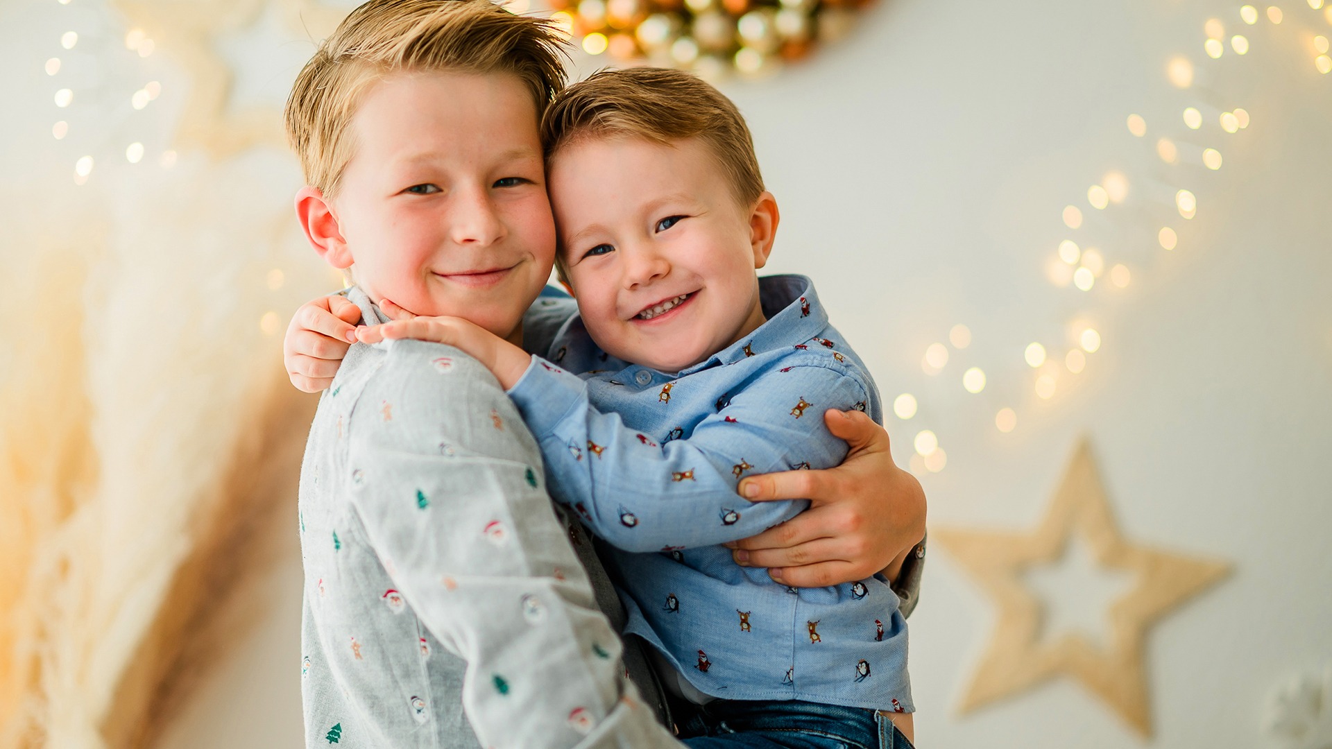 Two children hugging in front of a Christmas backdrop